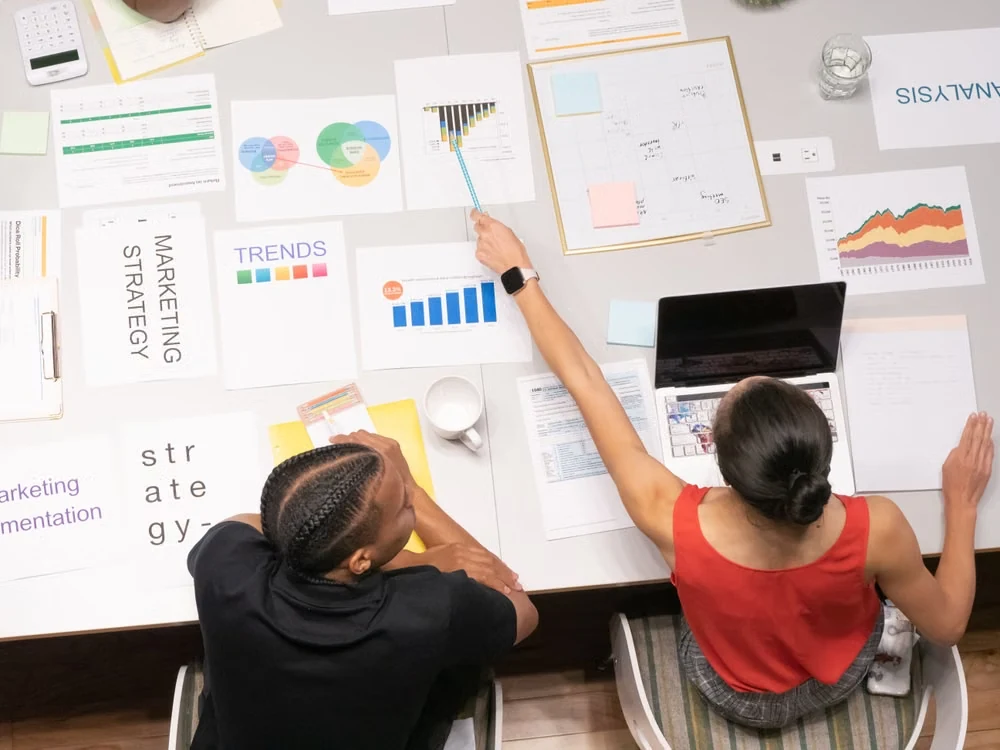 Two strategists working over marketing charts spread across a table