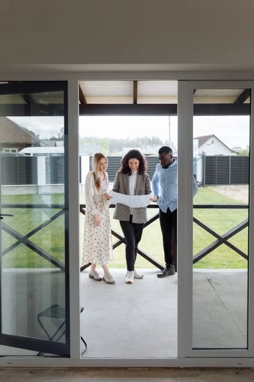 Three people reading a floor plan at the threshold of a new home